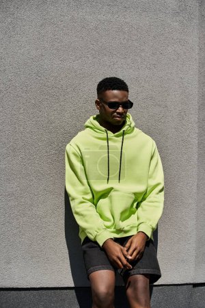 Photo for Stylish African American man in neon green hoodie leaning against a wall. - Royalty Free Image