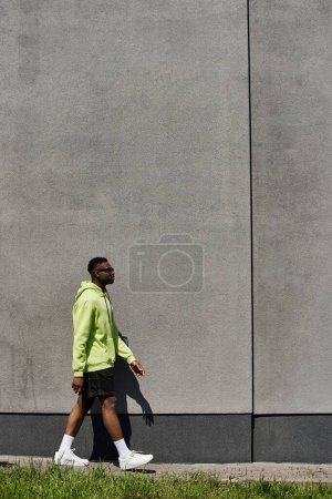 Ein modischer junger afroamerikanischer Mann, der vor einer grauen Wand läuft.