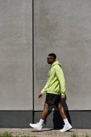 Modischer afroamerikanischer Mann in grünem Kapuzenpulli läuft die Straße entlang.