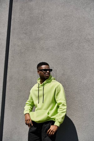 Photo for Stylish African American man in lime green hoodie leaning against a wall. - Royalty Free Image