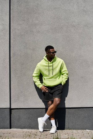 Handsome African American man in lime hoodie leaning against wall.
