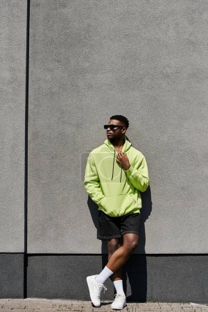 Stylish African American man in green hoodie leaning against a wall.