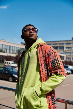 Handsome African American man in green hoodie and sunglasses balancing on railing.