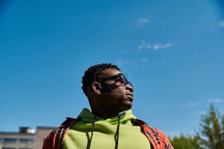 Handsome African American man in green hoodie gazes up at the sky.