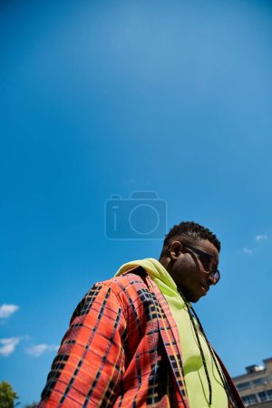 Handsome African American man in fashionable plaid jacket standing under a clear blue sky.