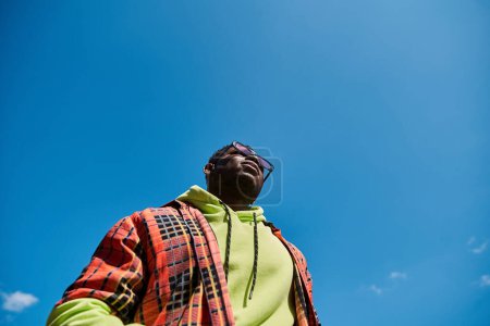 Schöner afroamerikanischer Mann in stylischer Jacke blickt in den Himmel.