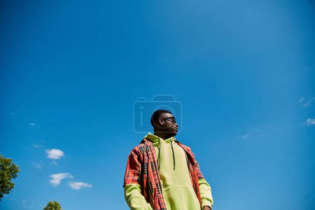 A fashionable African American man standing in a field under a blue sky.