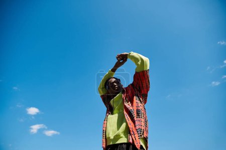 A fashionable young African American man standing in a field under a blue sky.