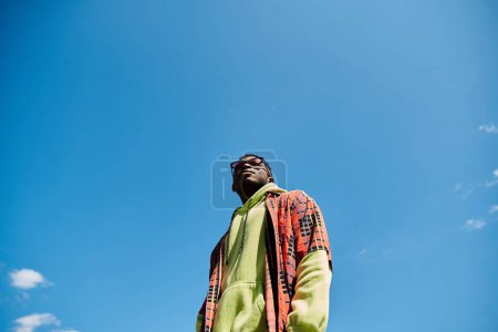 Handsome African American man in colorful jacket stands in lush field.