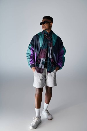 Elegante hombre afroamericano en chaqueta colorida y pantalones cortos posando con confianza.