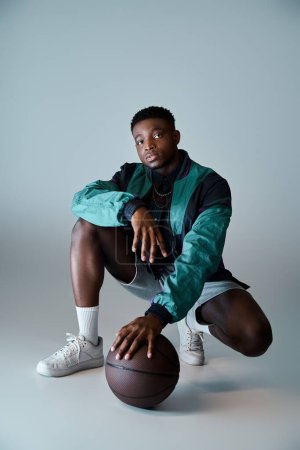 Young African American man in stylish attire crouching with a basketball ball.