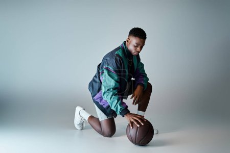 Fashionable young African American man in stylish attire crouching with basketball.