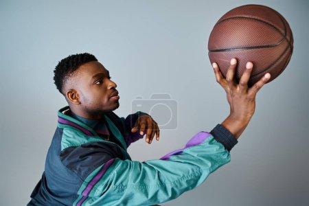 Ein modischer junger Afroamerikaner in stylischer Kleidung hält einen Basketball in der Hand.