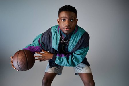 Téléchargez les photos : Jeune homme afro-américain élégant tenant un ballon de basket sur un fond gris. - en image libre de droit