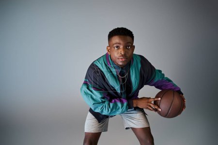Handsome African American man in stylish attire holding a basketball ball.
