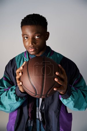 Handsome African American man in fashionable attire holding basketball on white background.