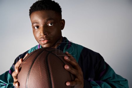 Handsome African American man in trendy attire holding up a basketball ball.