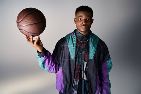 Fashionable African American man holding basketball against gray background.