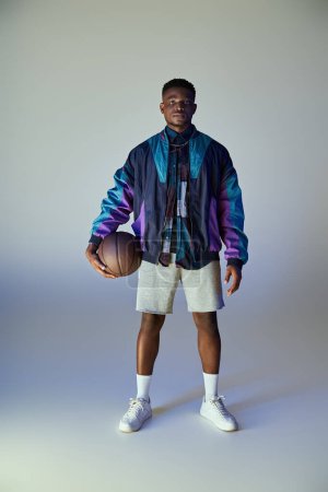 Téléchargez les photos : Jeune homme afro-américain à la mode tenant un ballon de basket devant un fond blanc. - en image libre de droit