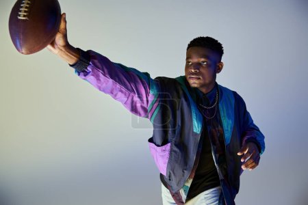 Photo for Young African American man in stylish purple jacket holds a football. - Royalty Free Image