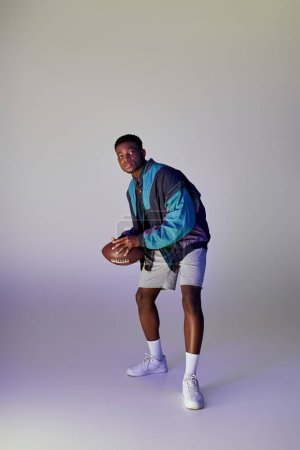 Téléchargez les photos : Handsome African American man poses with a football against a white backdrop. - en image libre de droit