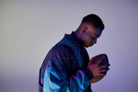 Photo for Young African American man in stylish attire holding a football. - Royalty Free Image