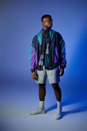 Handsome African American man in colorful jacket and shorts against blue backdrop.