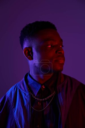 Photo for Handsome African American man in fashionable jacket and chain against vivid purple backdrop. - Royalty Free Image