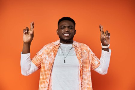A fashionable young African American man in an orange shirt is making a gesture with his hands.