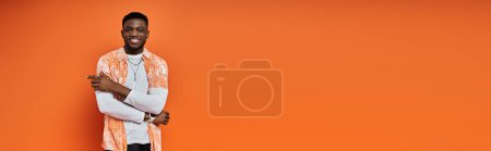 Foto de African American man posing stylishly in front of bright orange background. - Imagen libre de derechos