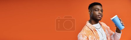 Téléchargez les photos : Beau Afro-Américain en tenue élégante tenant un café sur un fond orange. - en image libre de droit