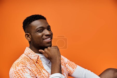 Téléchargez les photos : Handsome young man in orange shirt, seated on bright orange background. - en image libre de droit