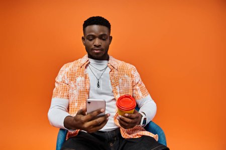 Téléchargez les photos : Young African American man sitting in chair, holding coffee cup. - en image libre de droit