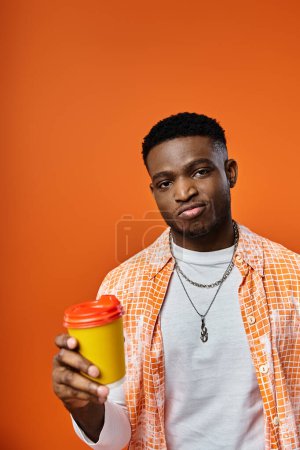 Foto de Joven sosteniendo taza de café contra fondo naranja vívido. - Imagen libre de derechos