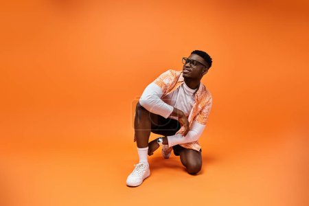 Fashionable African American man crouching on vibrant orange background.