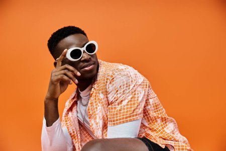 Photo for African American man in sunglasses sitting on orange background. - Royalty Free Image