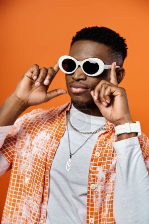 Handsome African American man in trendy sunglasses on vibrant orange background.