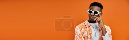 Photo for Handsome African American man in trendy sunglasses on vibrant orange background. - Royalty Free Image