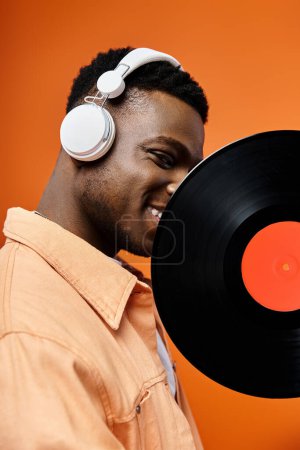 Elegante hombre afroamericano en auriculares sostiene disco de vinilo.