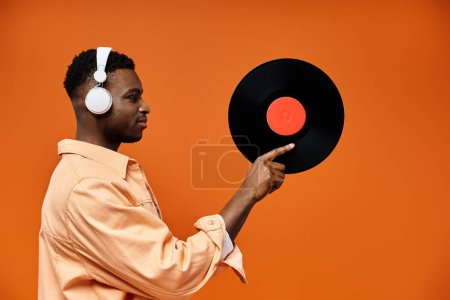Stylish man with headphones pointing at a record on vibrant orange background.