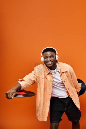 Handsome African American man in stylish attire holding a record on an orange background.