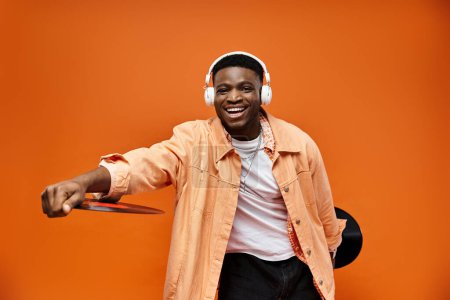 Photo for Stylish black man wearing headphones holding record on orange background. - Royalty Free Image