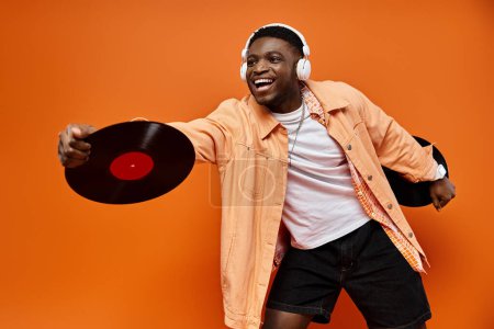 Black man with headphones holding a record on orange backdrop.