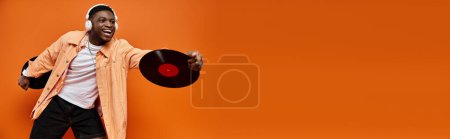 Homme afro-américain à la mode en tenue élégante tenant un record de vinyle sur fond orange vif.