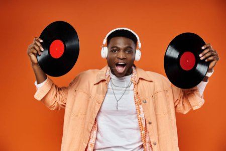 Téléchargez les photos : Stylish black man holding vinyl records against bright orange background. - en image libre de droit