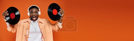Man holding two vinyl records against an orange backdrop.