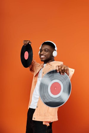 Stylish young African American man holding vinyl record on orange background.