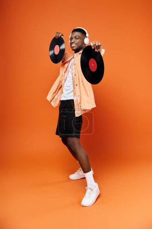 Handsome African American man holding vinyl record on orange backdrop.