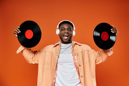 Stylish African American man holding vinyl records against orange backdrop.