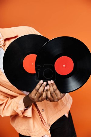Hombre afroamericano guapo sosteniendo dos discos de vinilo sobre un fondo naranja.